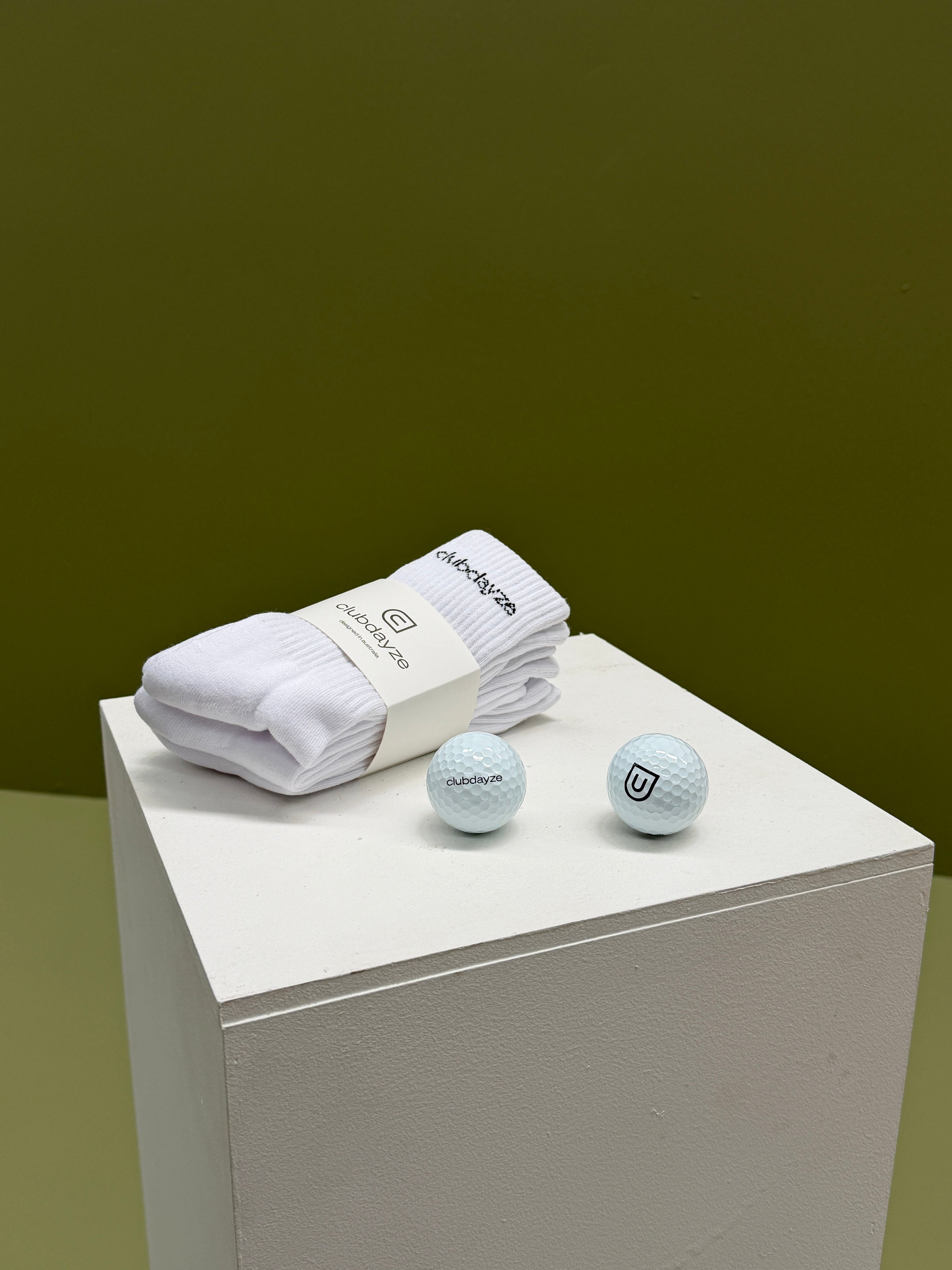 Cludayze logo white socks pack of 3 pairs, with two golf balls next to them on white surface 