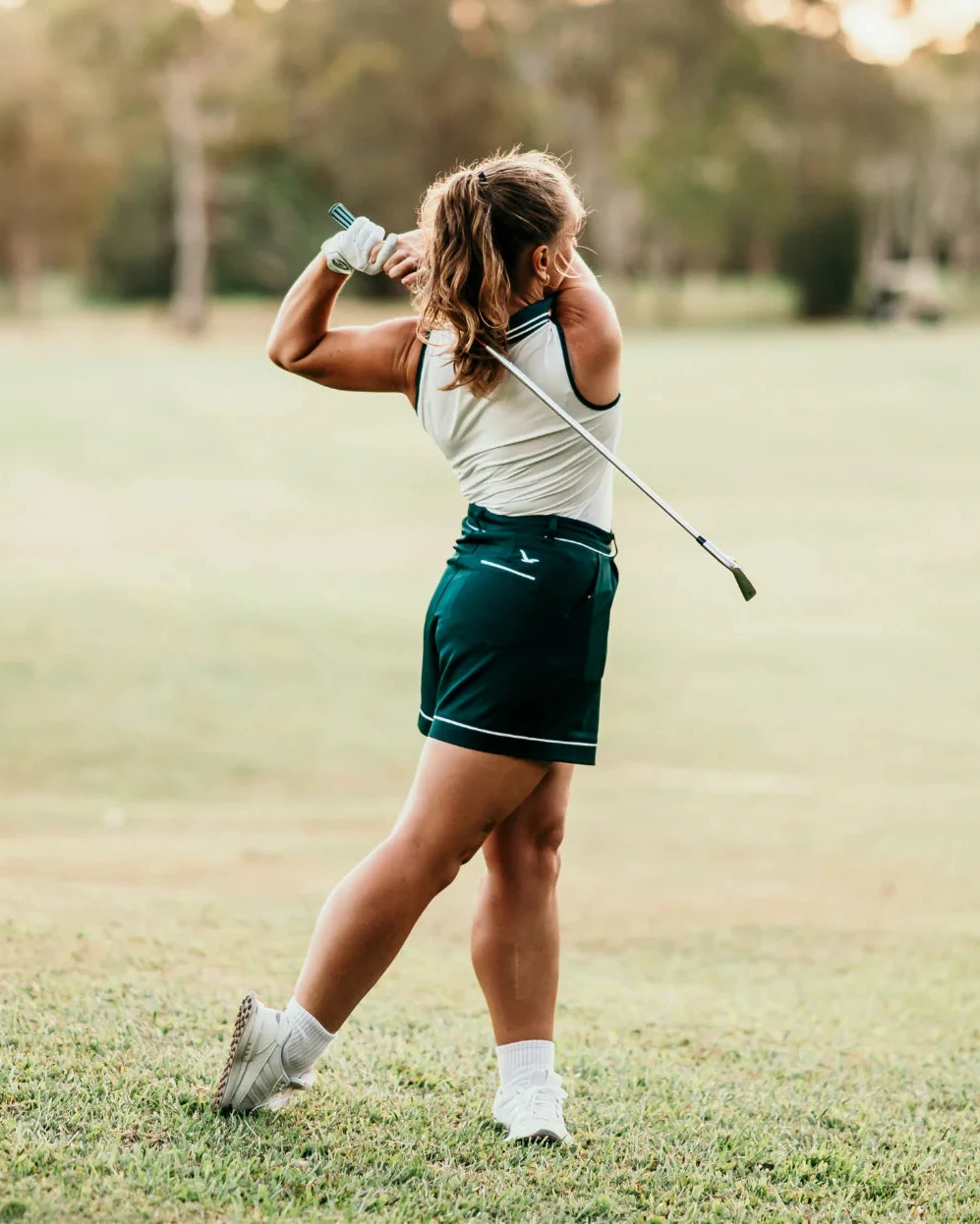 Woman playing golf on a grassy field with trees in the background
